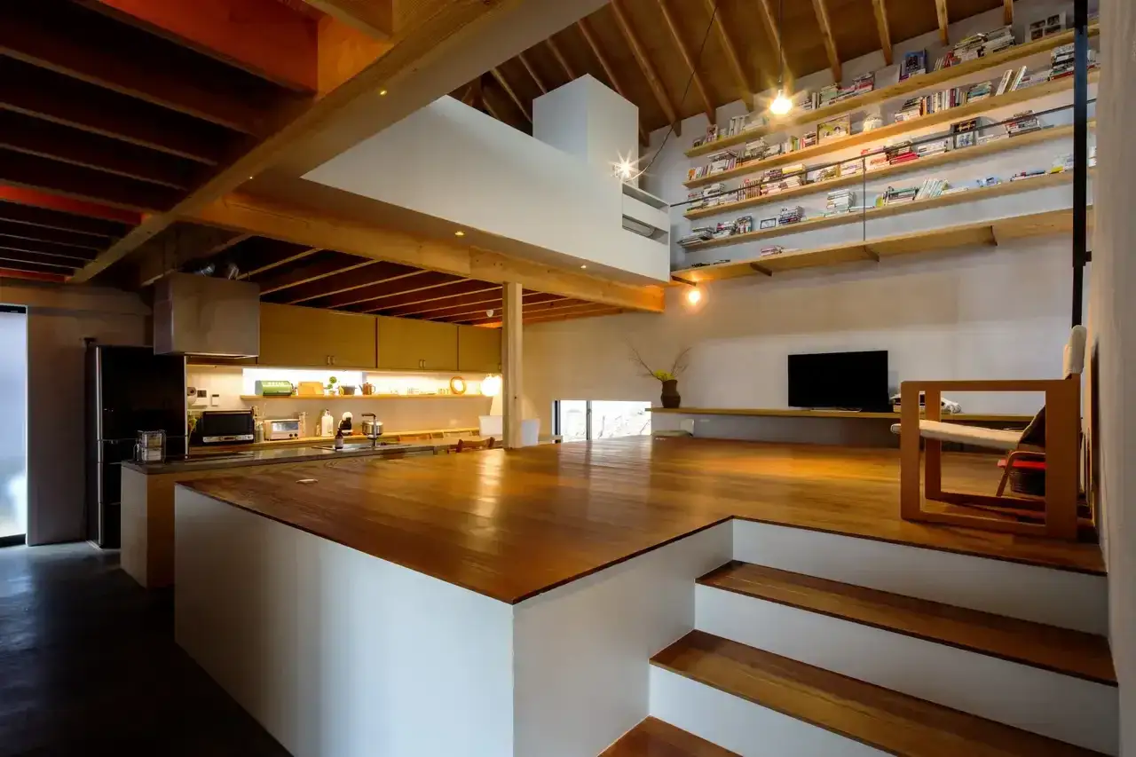 Int&eacute;rieur d'une maison inspiration japonaise, avec cuisine ouverte, salon sur&eacute;lev&eacute; et &eacute;tag&egrave;res remplies de livres.