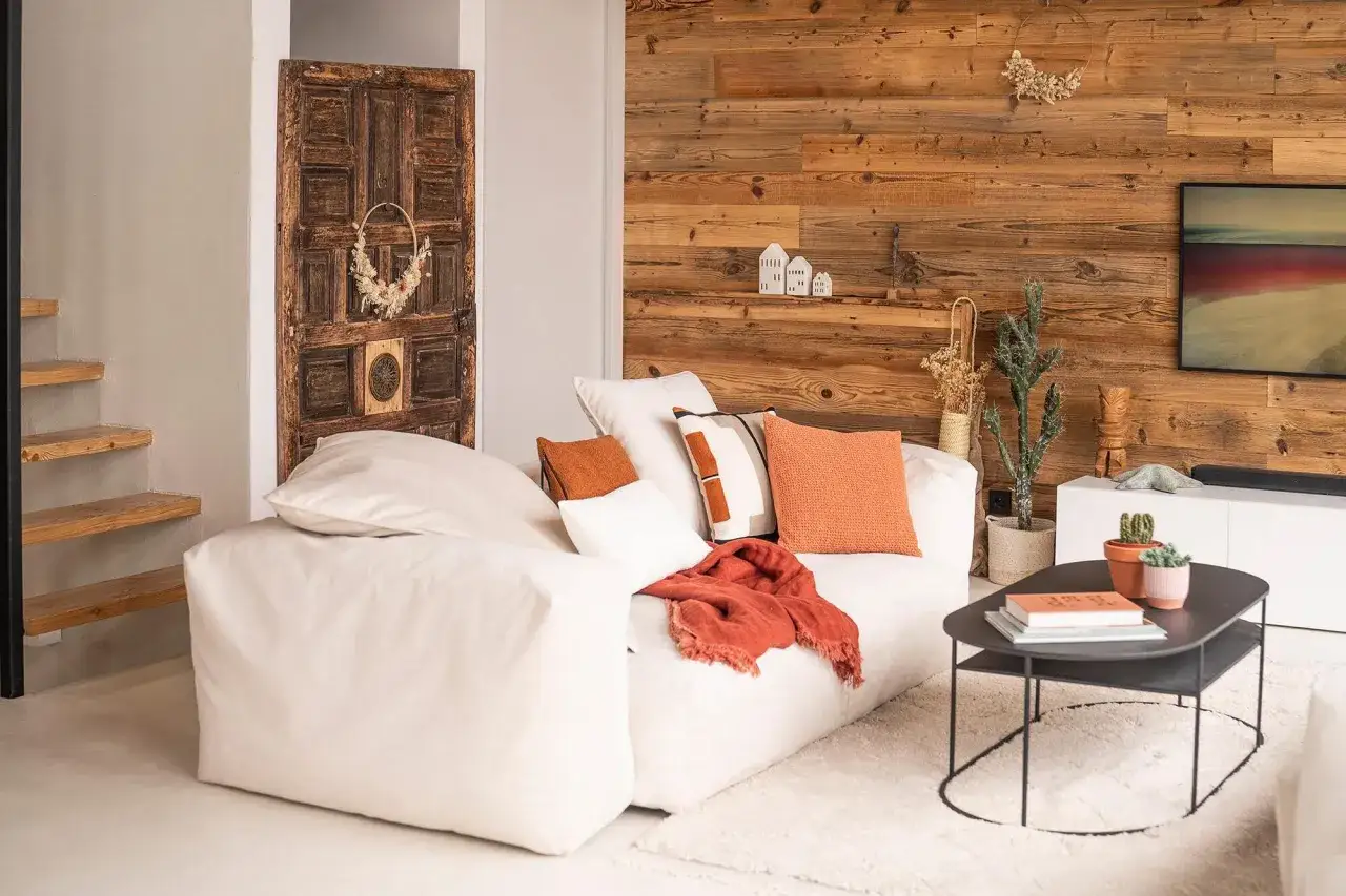 Un salon cosy avec un grand canap&eacute; blanc, des coussins orange et un plaid. Une porte ancienne d&eacute;core le mur.