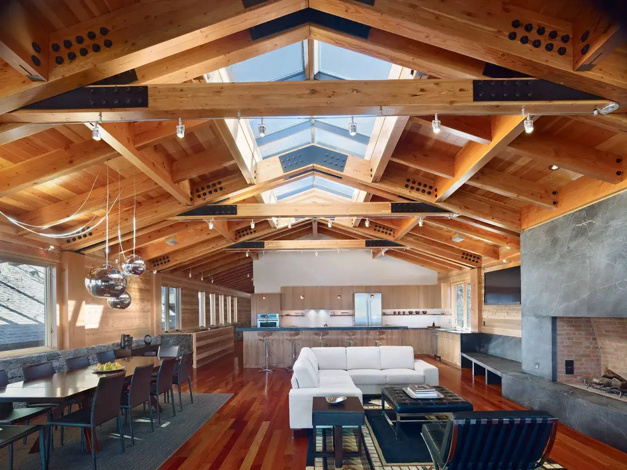 Vaste salon avec un plafond cath&eacute;drale moderne en bois, des poutres apparentes et des puits de lumi&egrave;re.