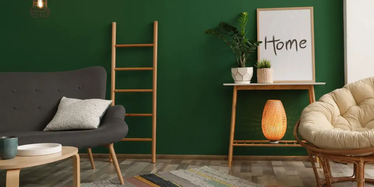 Un salon cosy avec un mur vert sapin. Un fauteuil gris, une &eacute;chelle en bois, une plante et un fauteuil rond en rotin cr&eacute;ent une ambiance chaleureuse. Quelle couleur avec du vert sapin ? Le beige et le bois s'harmonisent parfaitement.
