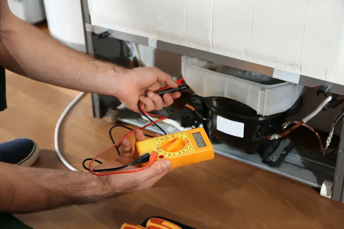 Un technicien v&eacute;rifie le compresseur d'un frigo qui claque avec un multim&egrave;tre.