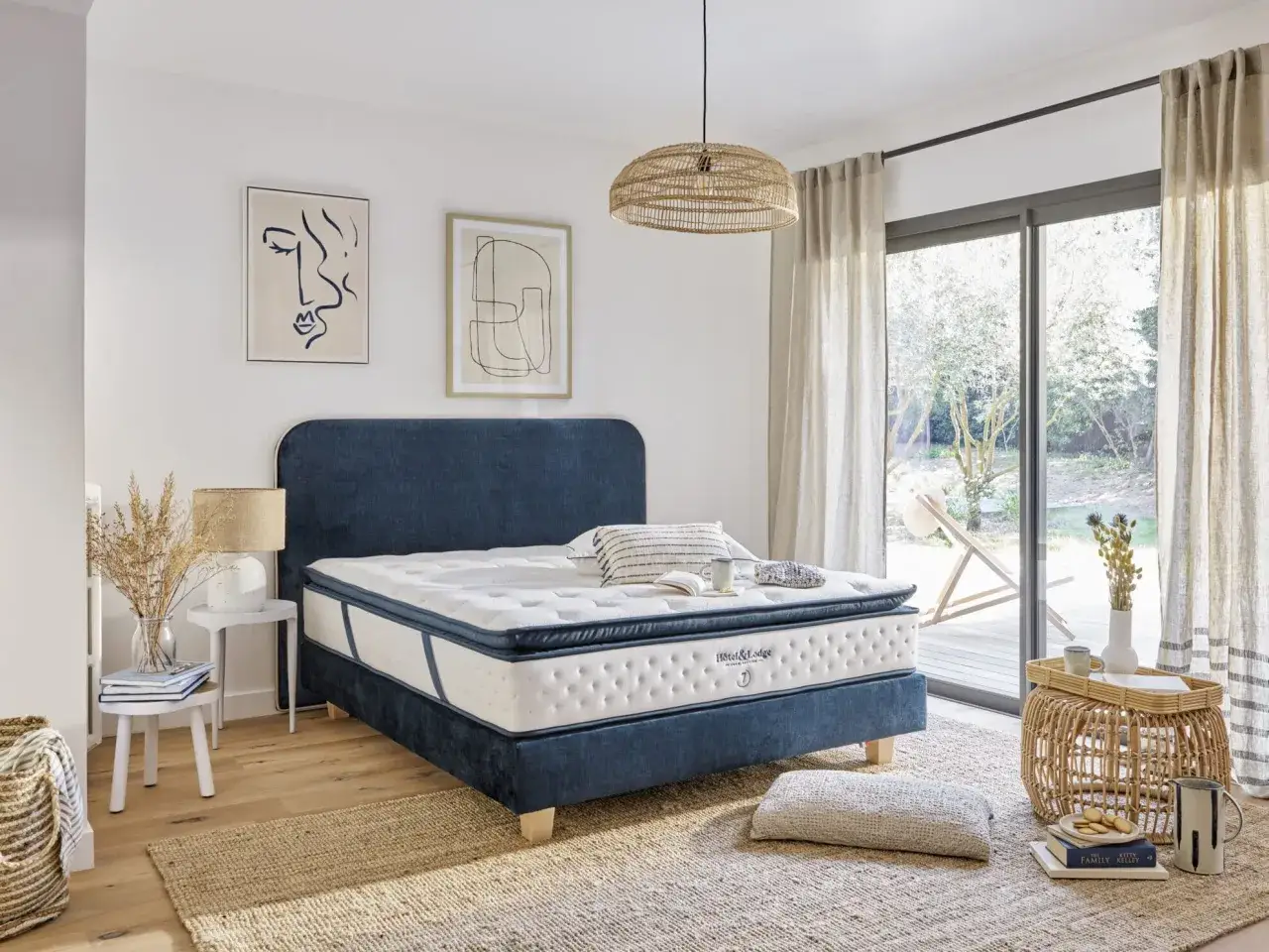 Chambre paisible avec un lit bleu profond et une bonne literie. Des tableaux abstraits et des rideaux clairs ajoutent une touche artistique.