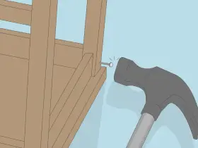 Un marteau s'apprête à frapper un clou dans la structure en bois d'un fauteuil qui grince.
