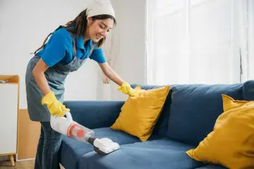 Femme nettoyant un canapé bleu avec un aspirateur pour éliminer la mauvaise odeur du tissu.