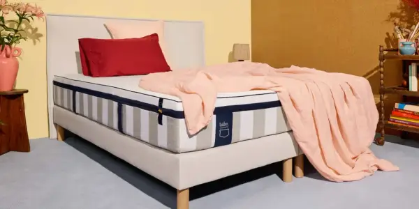 Un matelas rayé, drapé d'une couverture rose pâle, avec des coussins rouge et rose. La question est : combien de ressorts pour un bon matelas ?