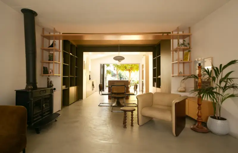Aménagement maison en longueur : salon avec poêle, étagères et vue sur salle à manger et jardin.