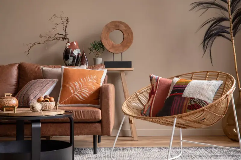Un salon cosy avec un canapé en cuir marron, des coussins aux motifs ethniques et une chaise en rotin.