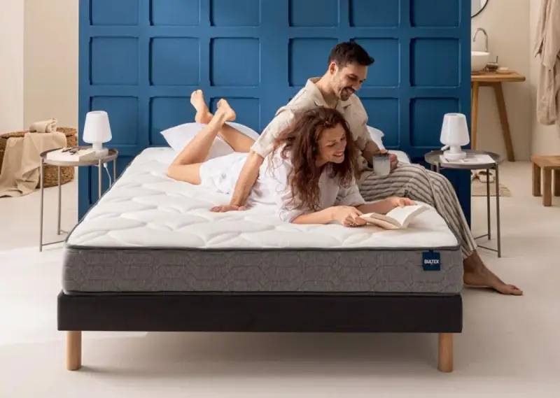 Un couple profite d'un moment de détente sur un matelas de taille lit 2 places. L'homme lit, la femme lit un livre.