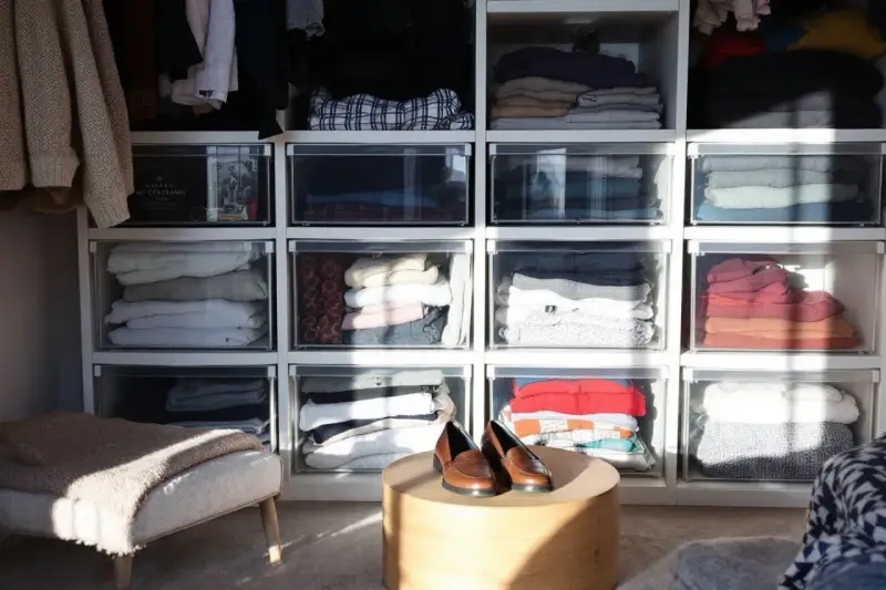 Des vêtements pliés dans des tiroirs transparents, une solution pour optimiser rangement vetements. Des chaussures marron sur une table basse.