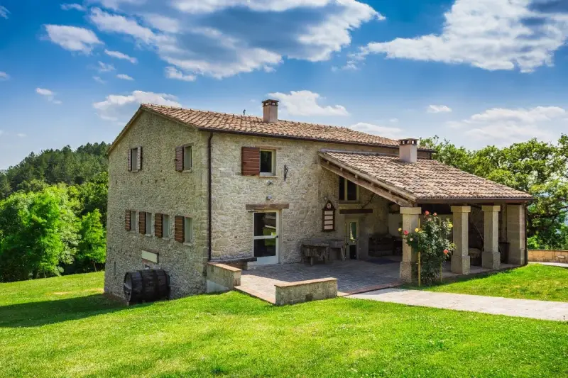 Belle ferme rénovée en pierre, entourée de verdure luxuriante sous un ciel bleu et nuageux.